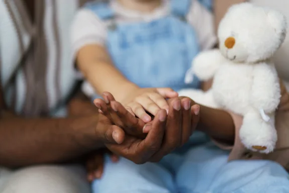 Adult hands gently cradling child's hand, showing care and togetherness with a teddy bear